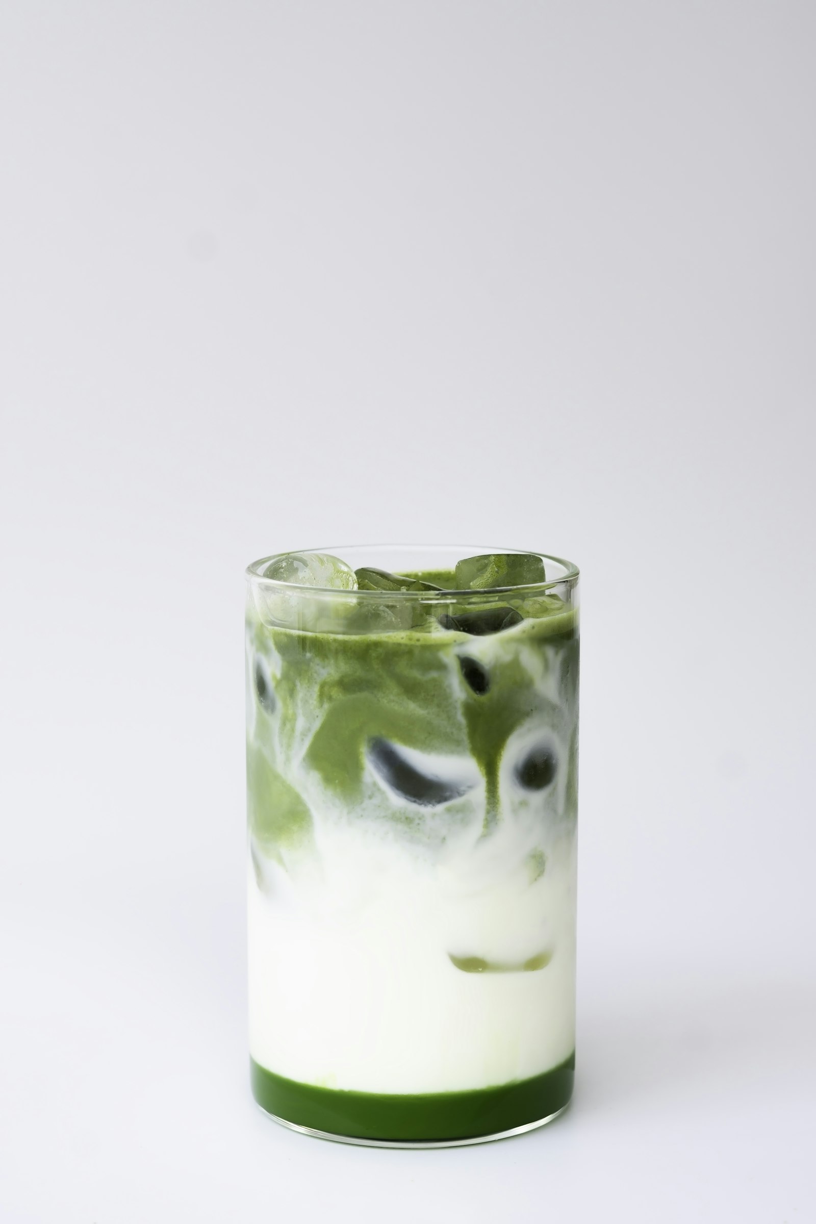 A glass of layered iced matcha latte on a plain white background