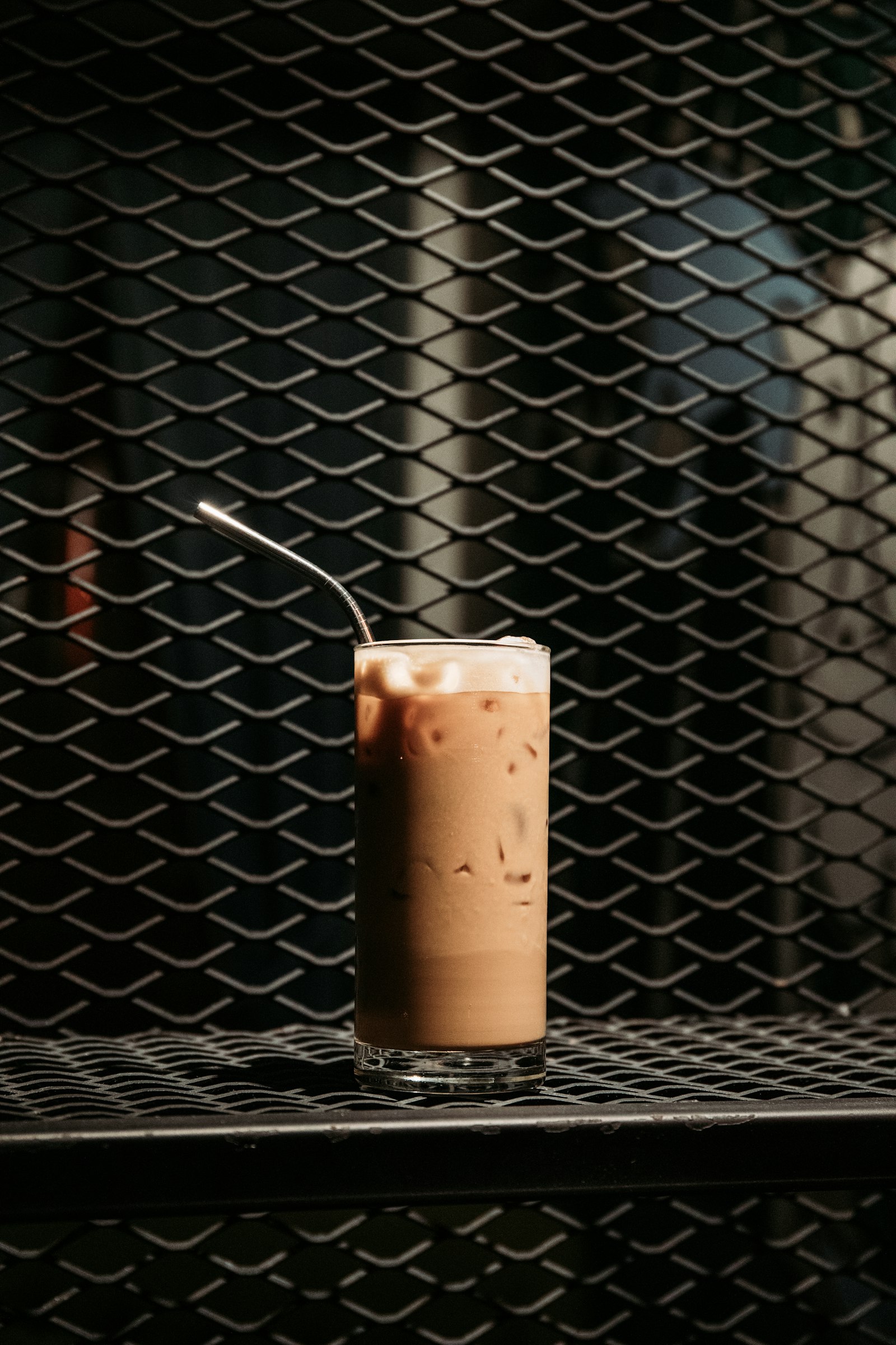 A tall glass of iced milk tea with a metal straw on a dark metal counter