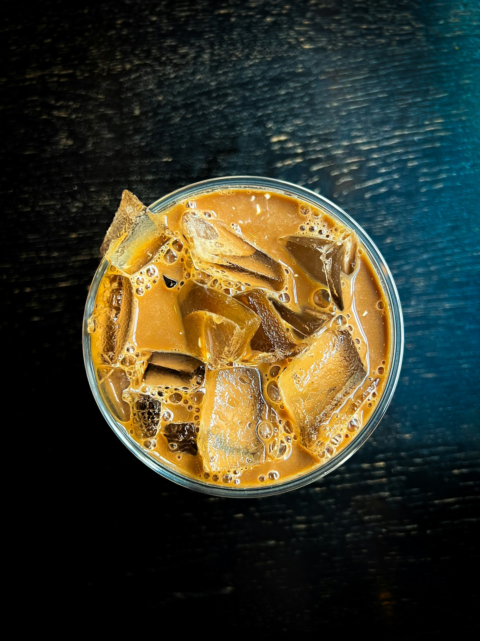 An overhead view of a glass of iced milk tea packed with ice and tapioca pearls